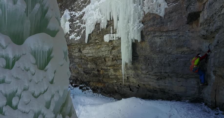 A person climbs up a rocky cliffside in the snowy wilderness