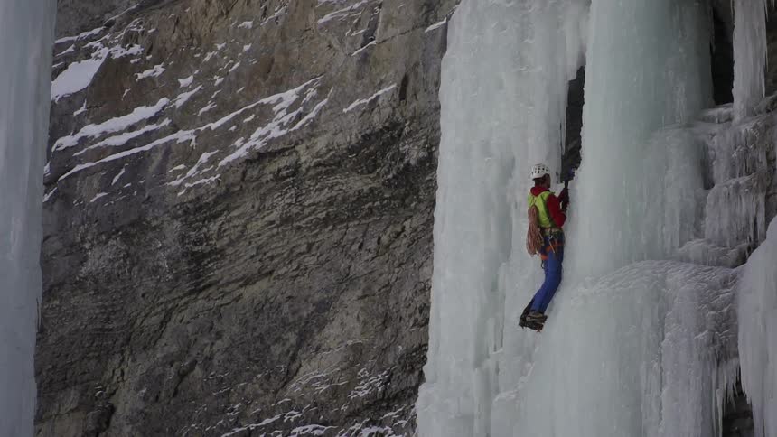 A man is slowly ascending a cliff covered with ice