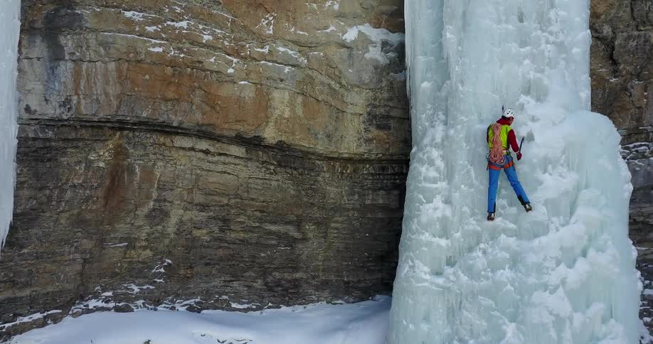 A man is climbing up ice by the side of a tall steep cliff