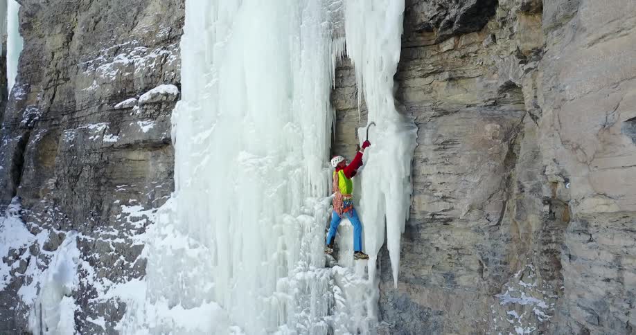 A man uses hooks to climb the ice on the cliff