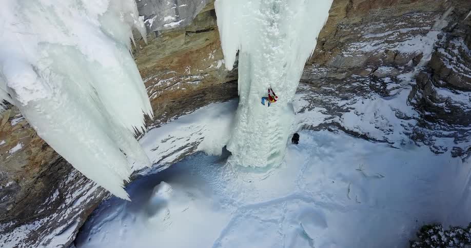 A man is climbing up ice on the side of a mountain