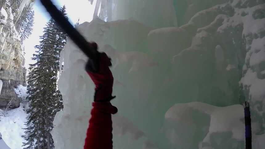 A man searches for a place to hook into the ice on the cliff