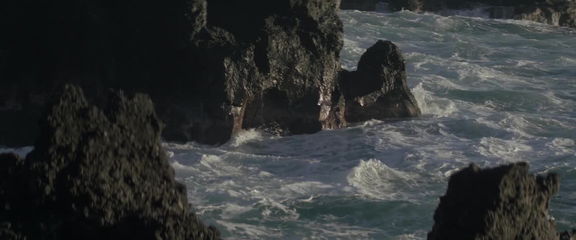 Waves crash against the tall jagged rocks