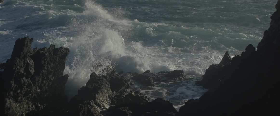 Ocean waves lap at rock outcroppings and splash into the air