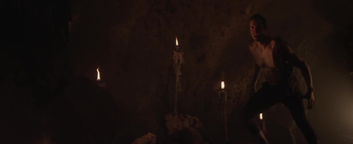 A man in a cave snarls at something and then rushes toward it