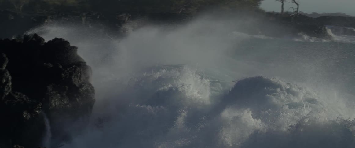 Tall waves crash against jagged rocks