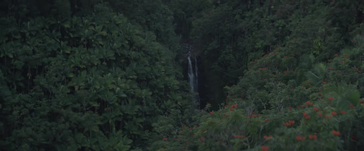 A waterfall is pouring behind the greens of the mountain sides