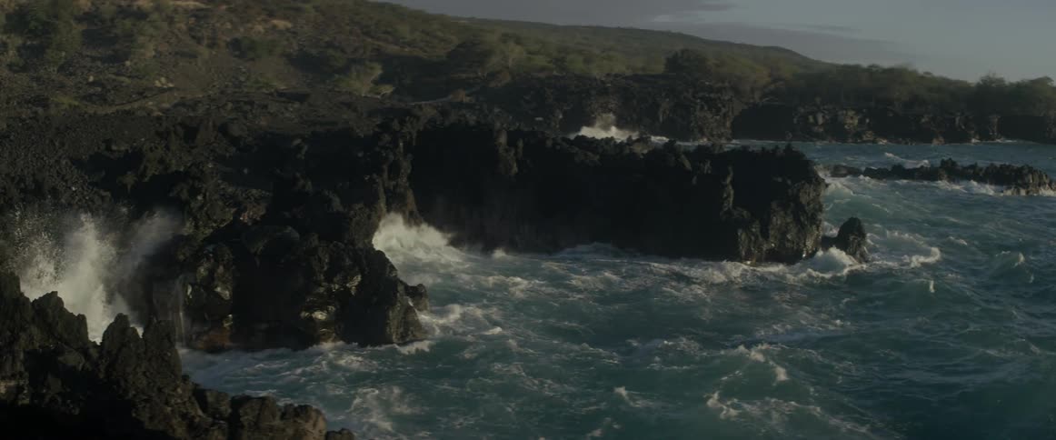 Waves crash against jagged rocks