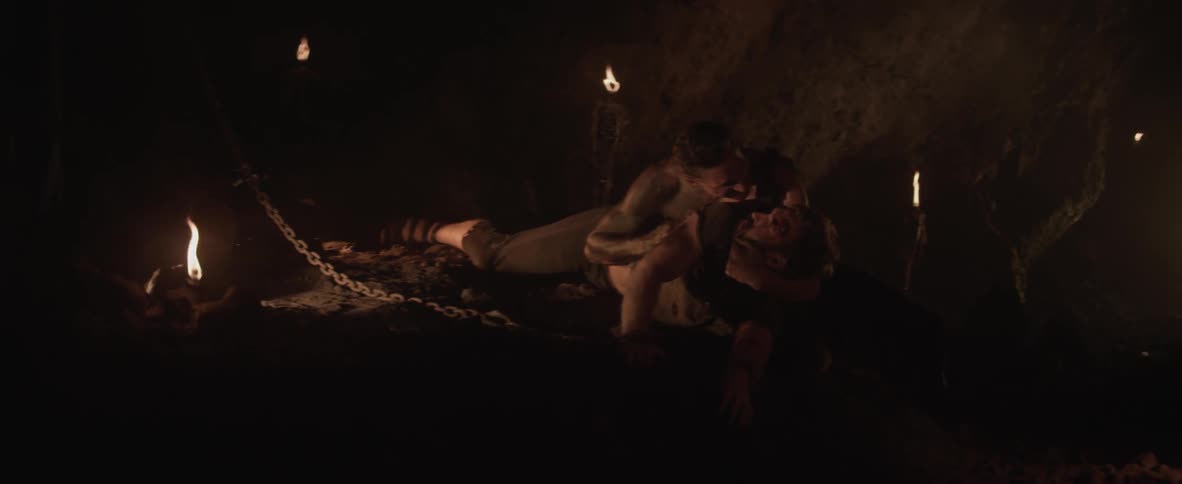 A man is holding another man down in a cave
