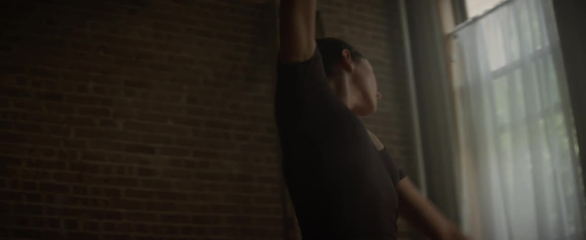 A woman is ballerina dancing by a brick wall