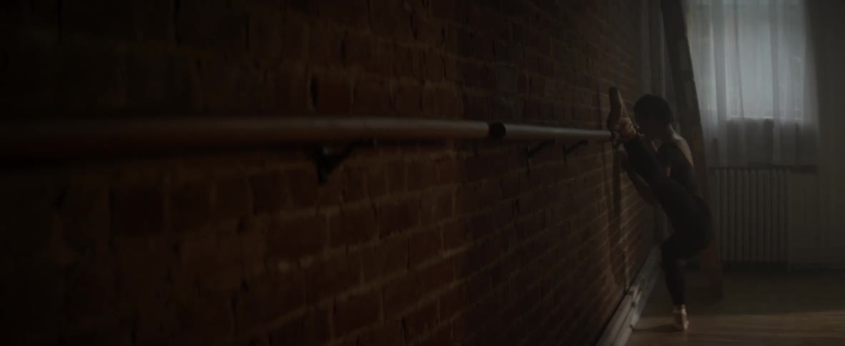 A ballerina is stretching her leg out on a bar