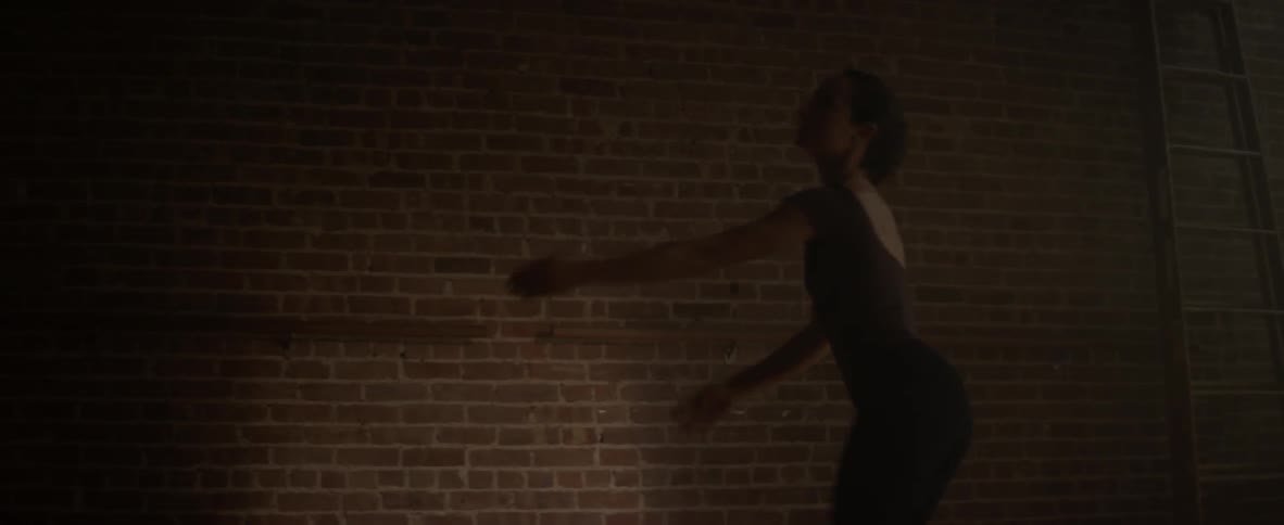A woman is jumping and dancing by a brick wall
