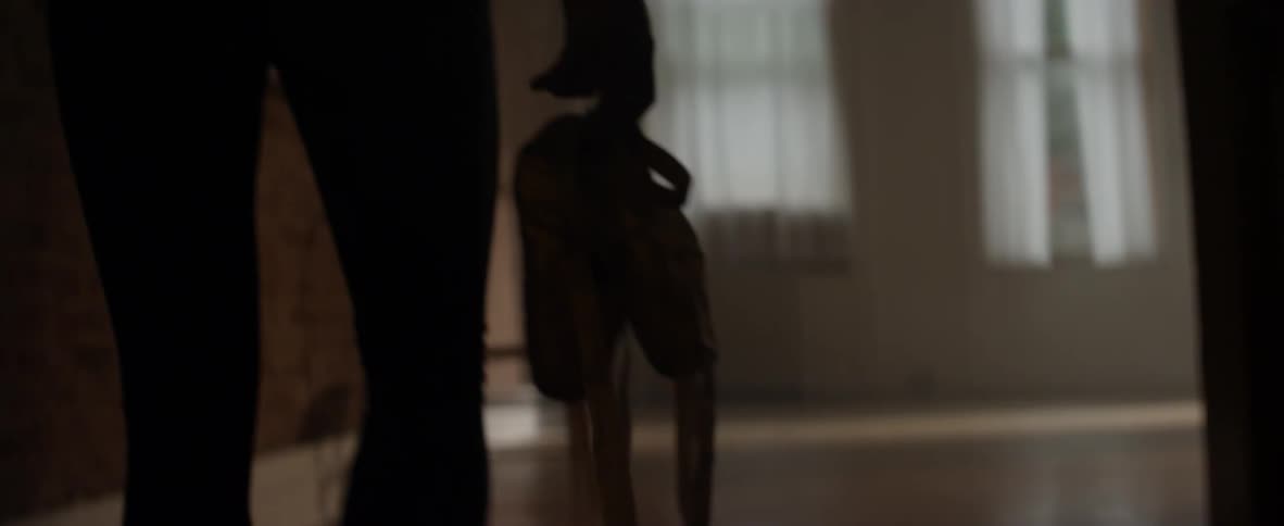 A ballerina carries pointe shoes into a studio