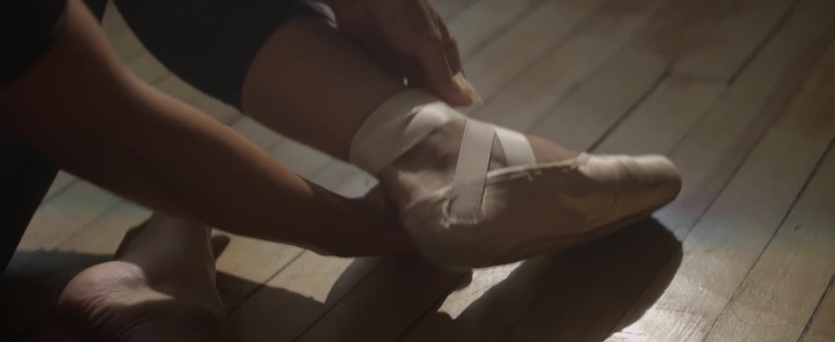 Person tying on some ballet slippers while sitting on the floor