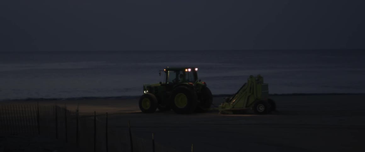 A tractor drives on a beach at night