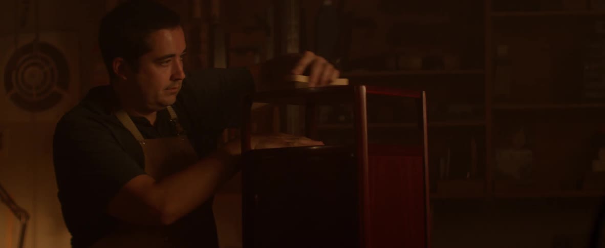 A carpenter brushes off a piece of furniture in a workshop