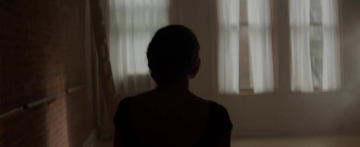 Woman walks towards a curtained window