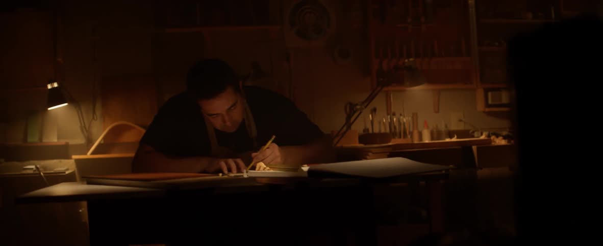 Man writes in a notebook at a desk in a dimly lit room