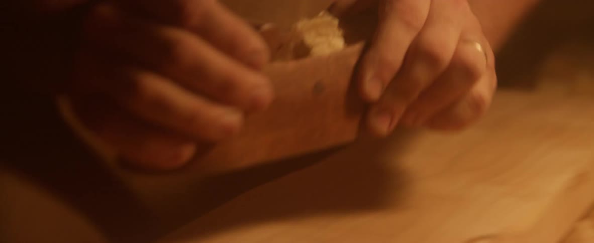 Person shaves a piece of wood smooth