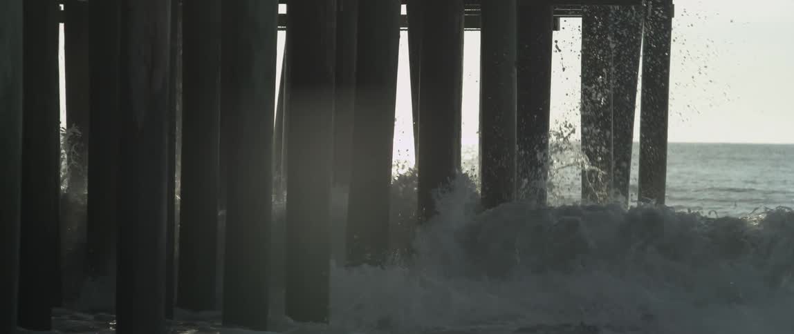 A large wave hits the wood holding up a pier