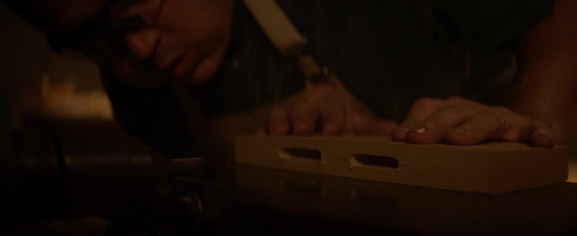 A carpenter blows sawdust from a workbench