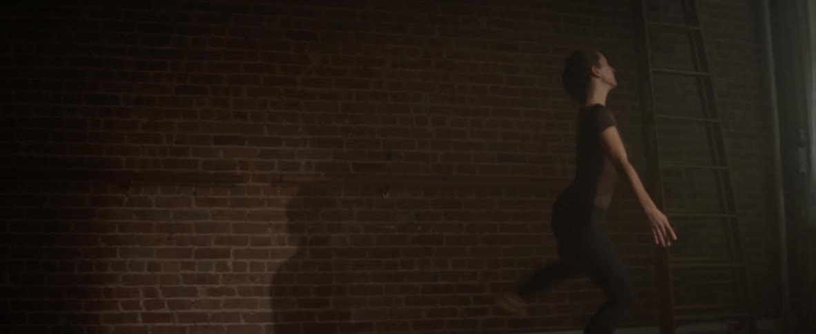 A woman jumps and dances past the brick wall