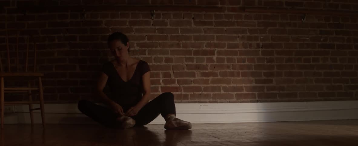 A dancer puts on ballet shoes and then stands
