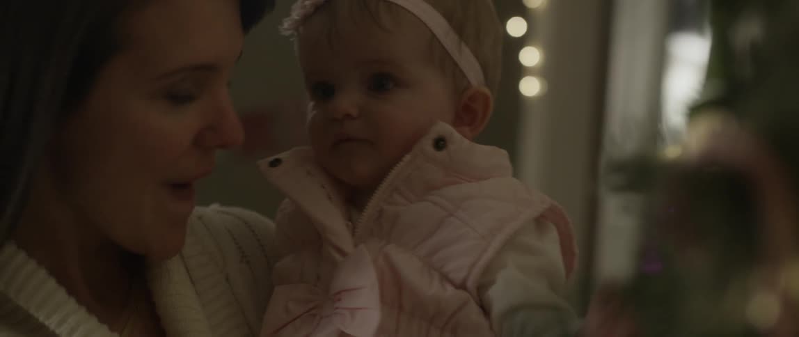 Baby sucks on a candy cane as her mother holds her