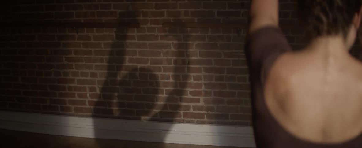 A woman is dancing with her shadow moving on the brick wall