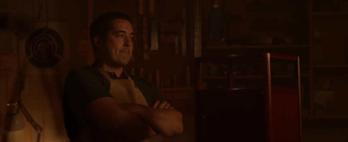 Man folds his arms and smiles in dim light