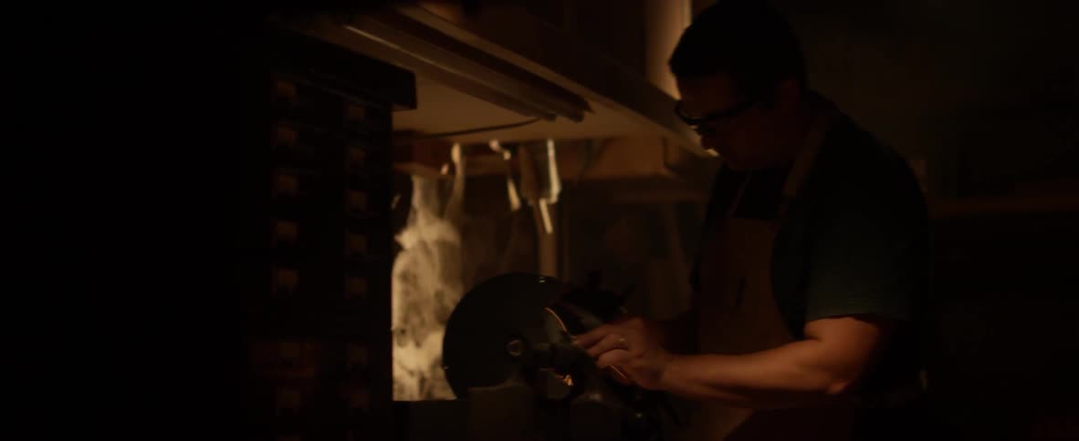 Sparks coming off some material that a man is holding against a spinning device in a dark area