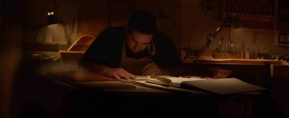Man writes in a notebook on a desk in a dimly lit room