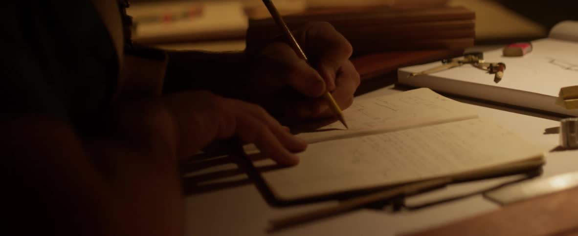 Person sitting at desk writing with pencil in notebook