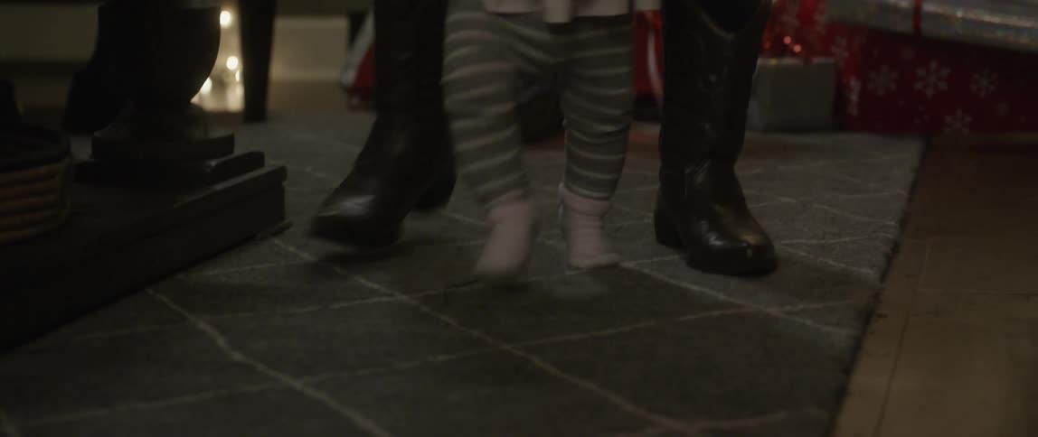 Woman helping baby walk beside a christmas tree