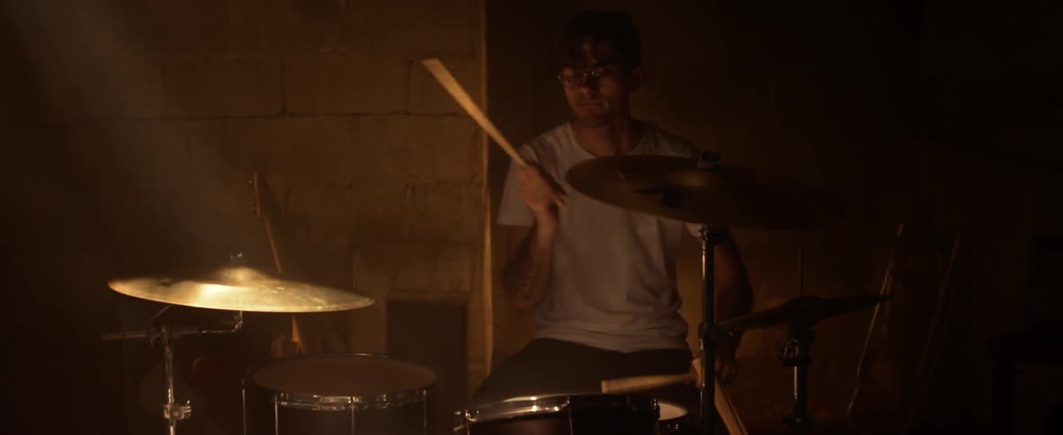 A man is playing drums wearing a white t-shirt