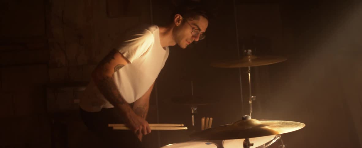 A man enters the room and sits down by the drums