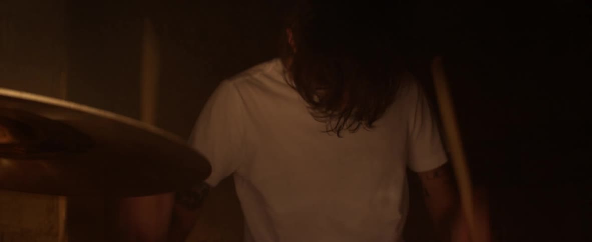 Drummer in a white t-shirt hits cymbals with his drumsticks