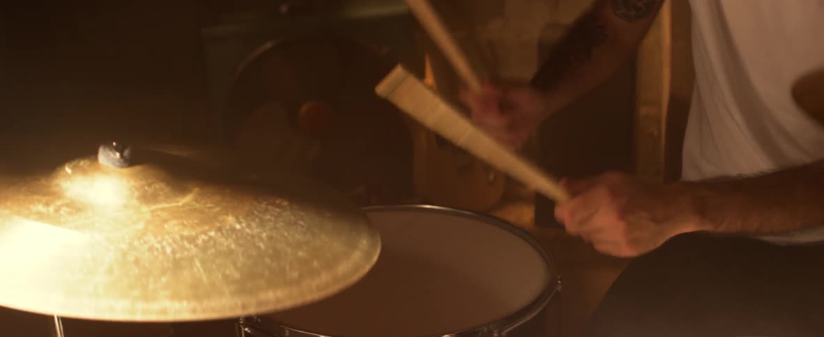 Man in a white shirt hits a cymbal with drumsticks