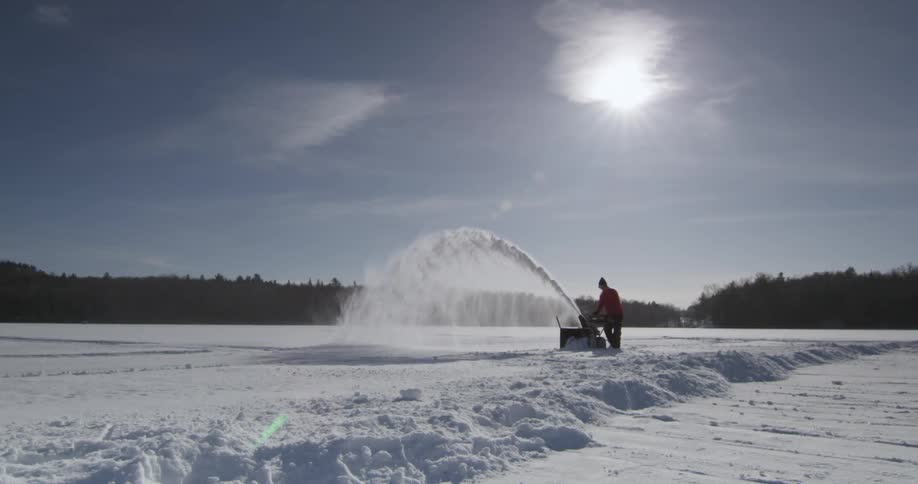 Man using a snow blower to clear an area on a cloudy day