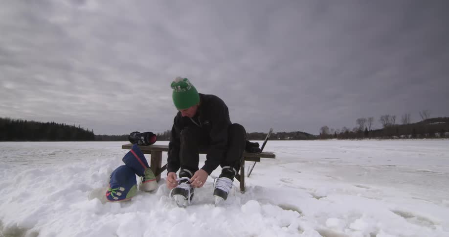Man lacing up his skates sitting on a bench in the snow
