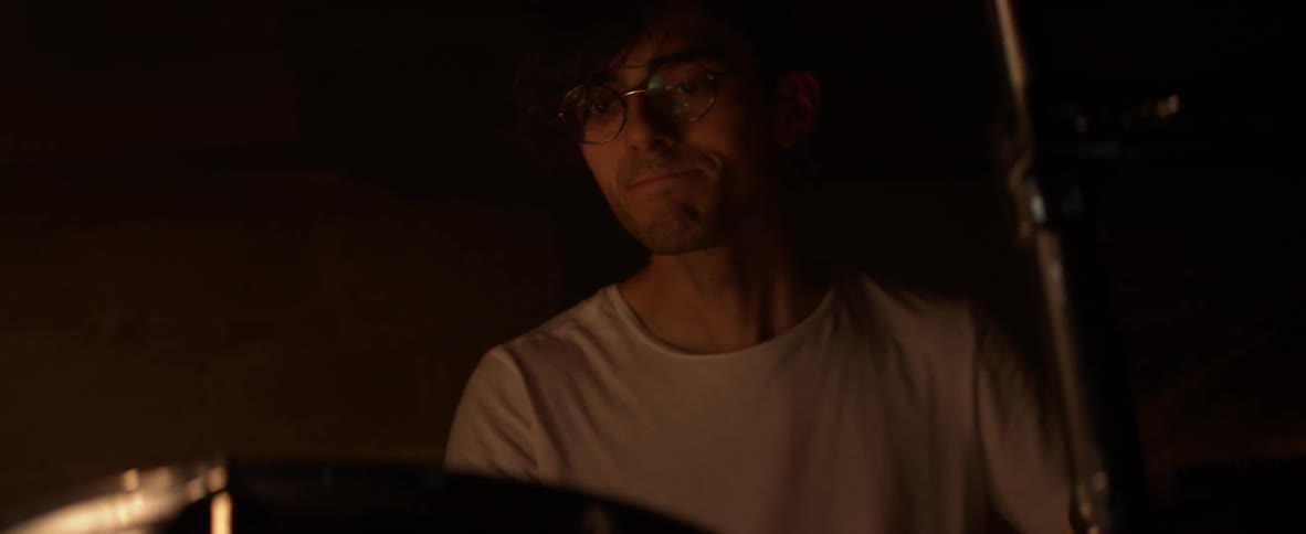 A man wearing glasses is playing drums