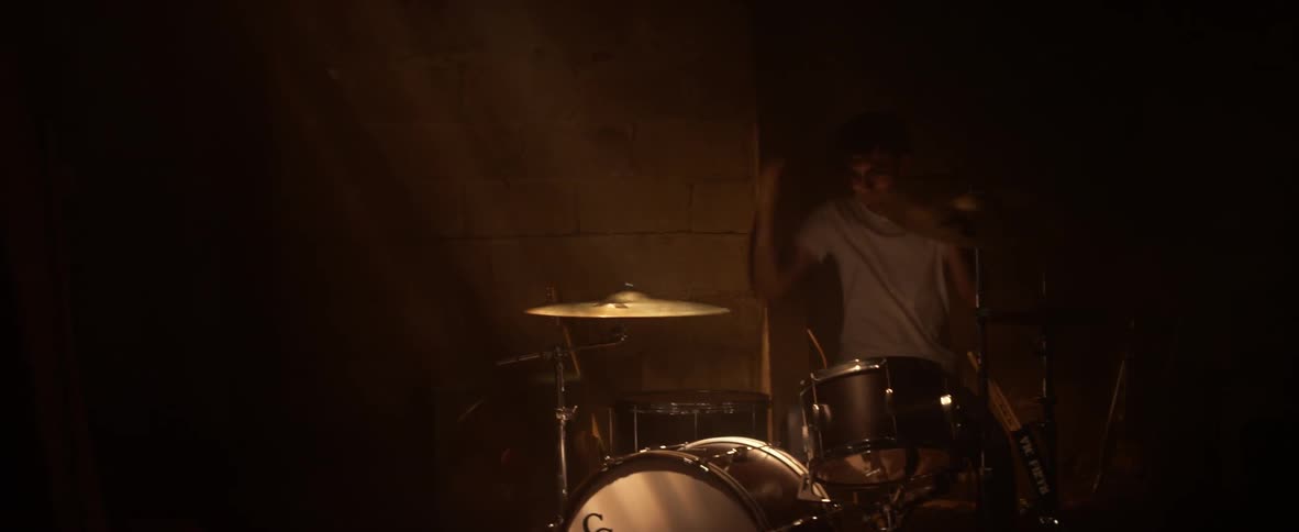 A man plays the drums in a dim room