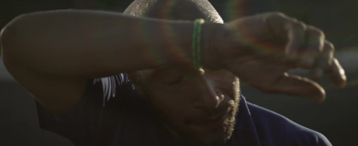 A man standing in the sun wipes his brow with his arm