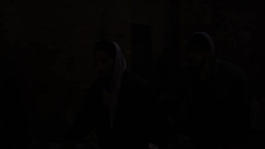 People stand near a fire in a barrel at night