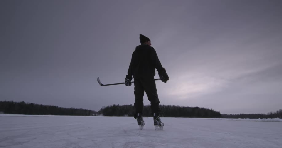 Man on skates holding hockey sticks below a cloudy sky