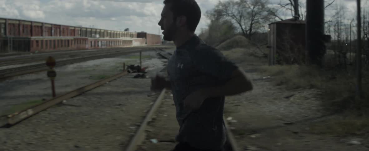 A man is jogging over train tracks through an industrial area
