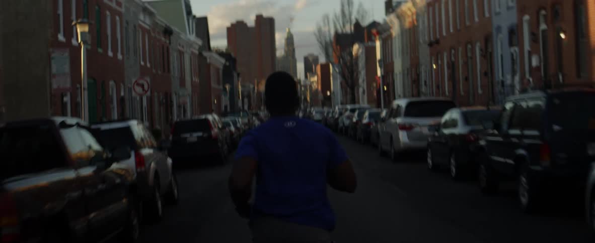 A man jogs on a city street lined with cars