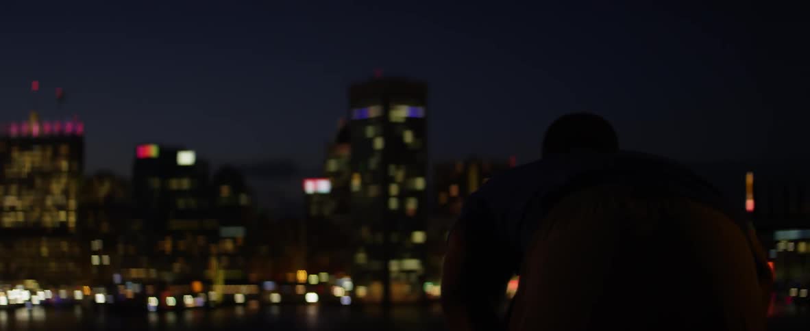 Silhouette of a person walking at night with a lit up city in the background