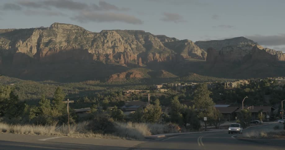 A vehicle drives on a road through a town with mountains in the distance