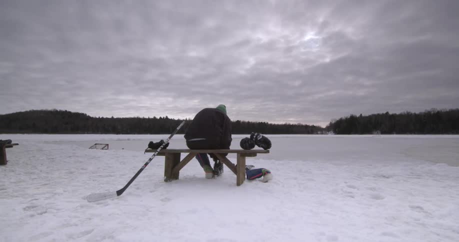 A man sits on a bench in the snow and puts on his skates